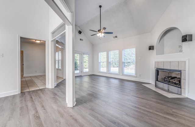 unfurnished living room with french doors, ceiling fan, high vaulted ceiling, hardwood / wood-style flooring, and a tile fireplace