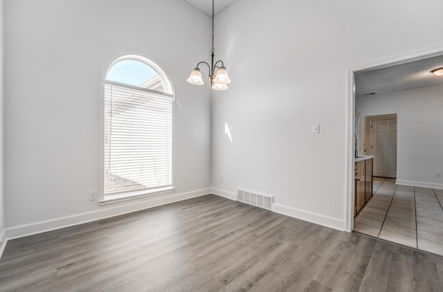 spare room with hardwood / wood-style flooring, high vaulted ceiling, and an inviting chandelier