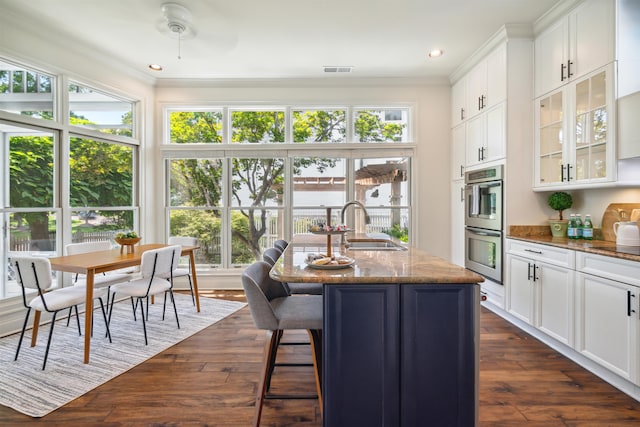 kitchen with an island with sink, white cabinets, dark wood-type flooring, and dark stone countertops