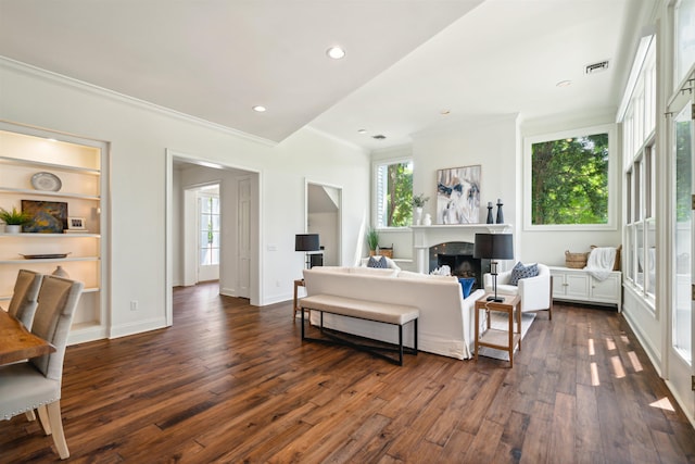 living room featuring dark hardwood / wood-style floors, built in features, crown molding, and a healthy amount of sunlight