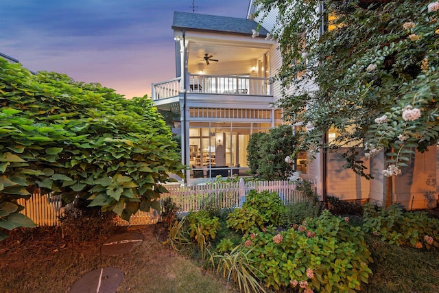 back house at dusk featuring ceiling fan and a balcony