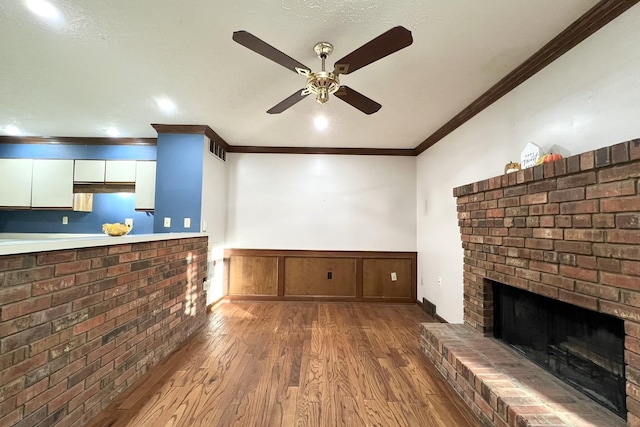 unfurnished living room featuring crown molding, a brick fireplace, dark wood-type flooring, and ceiling fan