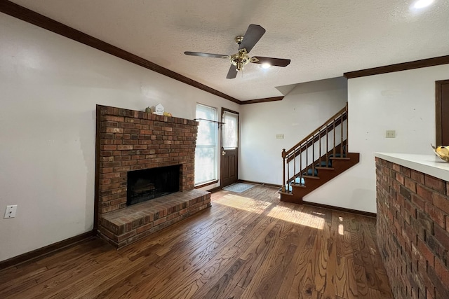 unfurnished living room featuring wood-type flooring, ceiling fan, crown molding, a brick fireplace, and a textured ceiling