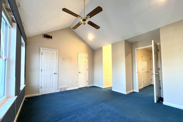 unfurnished bedroom with vaulted ceiling, dark colored carpet, ceiling fan, multiple closets, and a textured ceiling