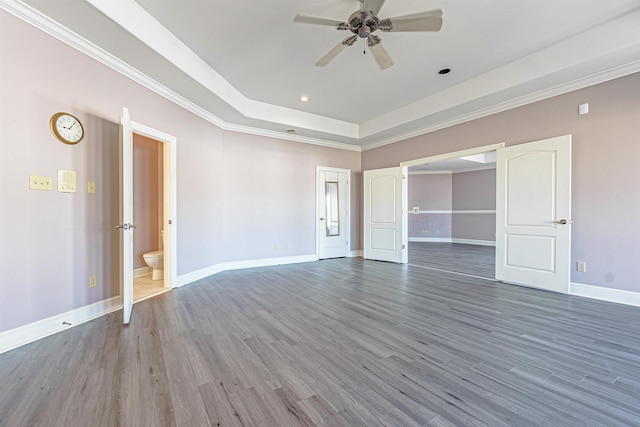 interior space with dark wood-type flooring, connected bathroom, ceiling fan, and a raised ceiling