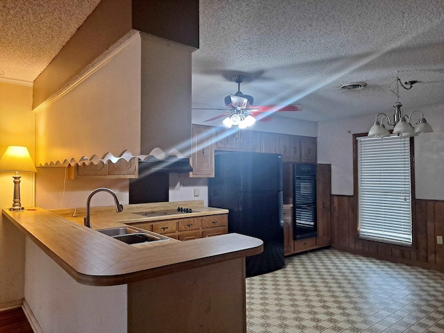 kitchen featuring sink, wooden walls, black appliances, ceiling fan with notable chandelier, and kitchen peninsula