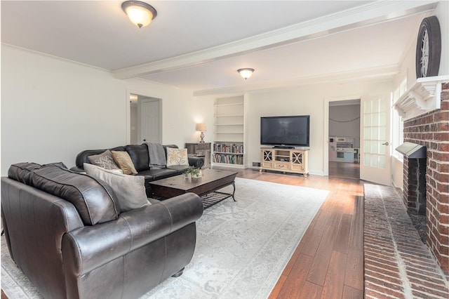 living room featuring built in shelves, a brick fireplace, ornamental molding, beamed ceiling, and hardwood / wood-style floors