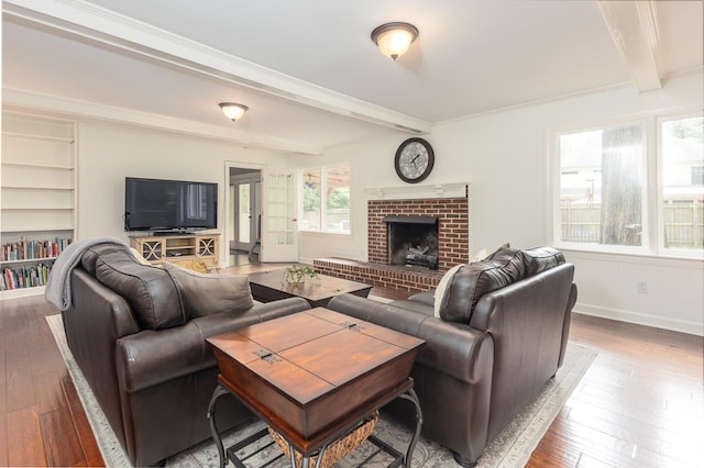 living room with built in features, hardwood / wood-style floors, beam ceiling, ornamental molding, and a brick fireplace