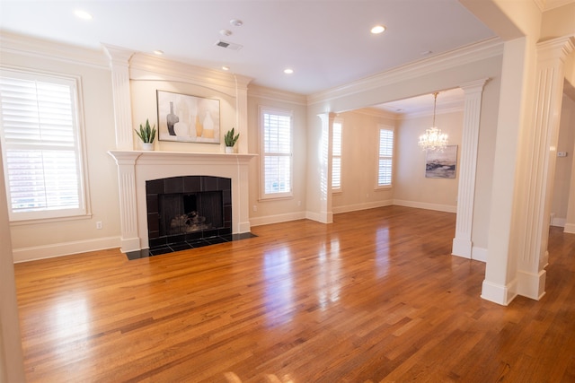 unfurnished living room featuring crown molding, plenty of natural light, a tiled fireplace, and ornate columns