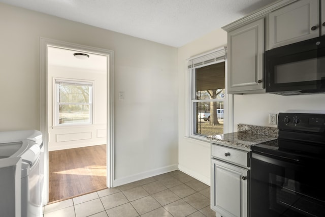 kitchen featuring light tile patterned floors, gray cabinetry, independent washer and dryer, black appliances, and stone countertops