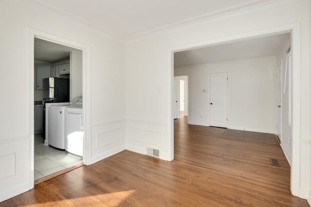 empty room with ornamental molding, separate washer and dryer, and light hardwood / wood-style floors