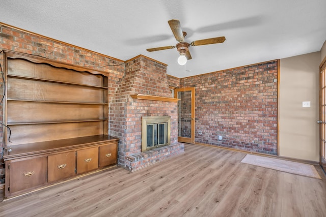 unfurnished living room featuring brick wall, a fireplace, light wood-type flooring, ceiling fan, and a textured ceiling