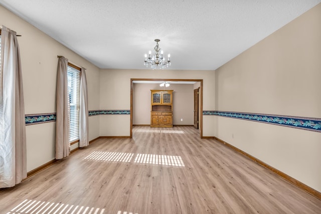 empty room featuring a textured ceiling, a chandelier, and light wood-type flooring