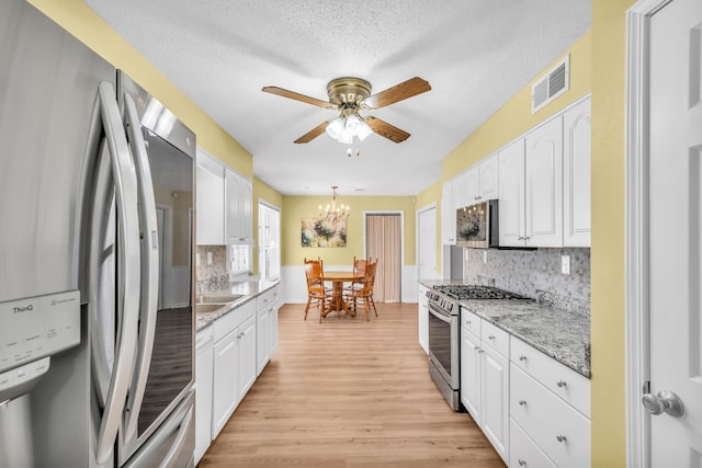 kitchen with appliances with stainless steel finishes, white cabinets, backsplash, hanging light fixtures, and light stone counters