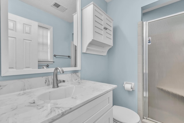 bathroom featuring toilet, vanity, a textured ceiling, and walk in shower