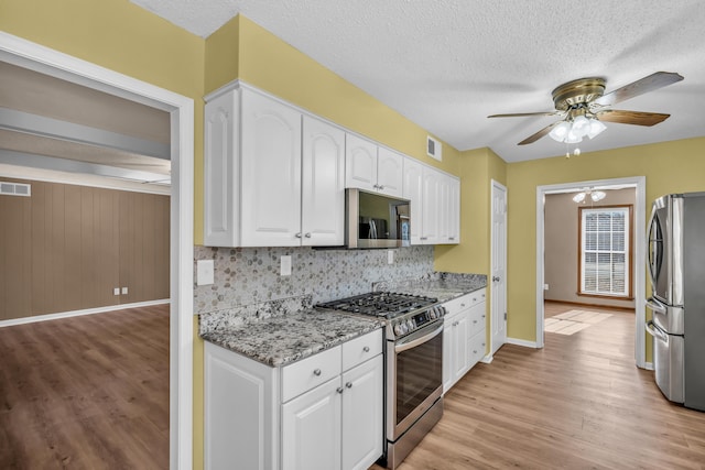 kitchen with appliances with stainless steel finishes, tasteful backsplash, white cabinetry, light stone counters, and light hardwood / wood-style flooring