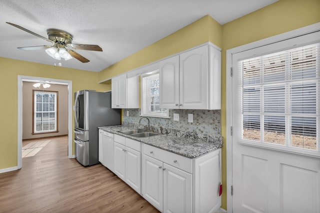 kitchen with stainless steel refrigerator, white cabinetry, sink, decorative backsplash, and light stone countertops