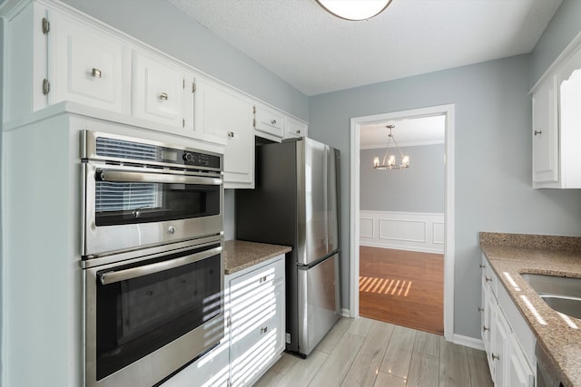 kitchen featuring white cabinetry, sink, a notable chandelier, stainless steel appliances, and light stone countertops