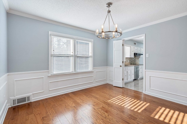 unfurnished dining area featuring an inviting chandelier, light hardwood / wood-style flooring, ornamental molding, and a textured ceiling