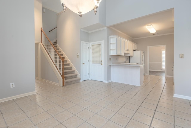 kitchen with white cabinetry, ornamental molding, light tile patterned flooring, kitchen peninsula, and white fridge