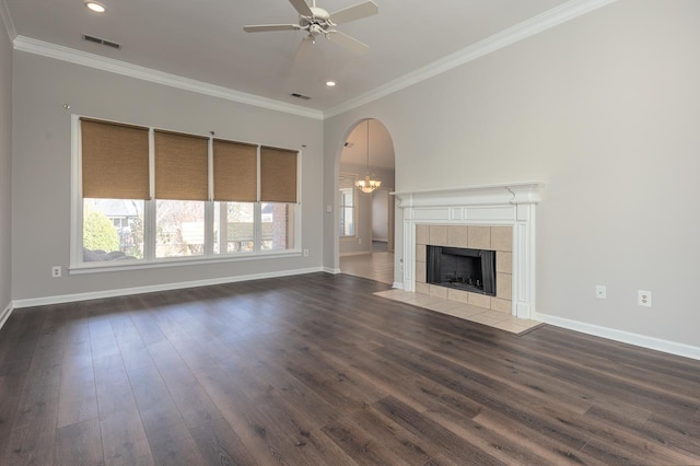 unfurnished living room with a tiled fireplace, ceiling fan with notable chandelier, dark wood-type flooring, and crown molding