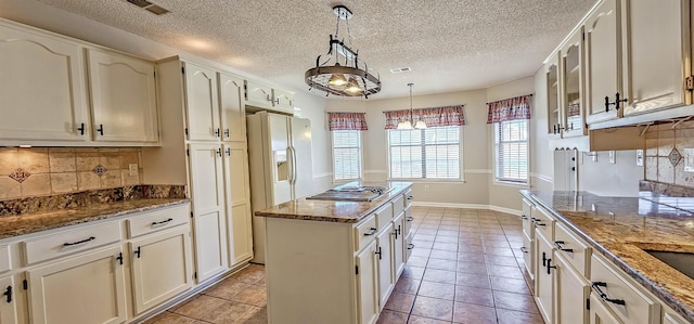 kitchen with stone counters, light tile patterned flooring, decorative light fixtures, a center island, and stainless steel gas cooktop