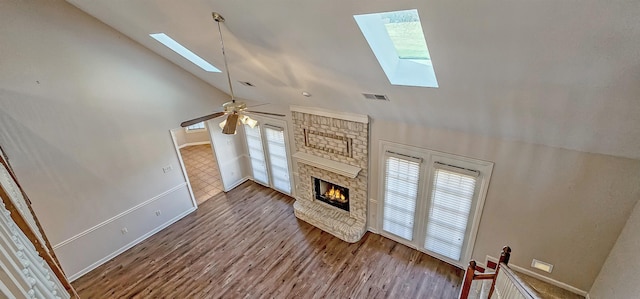 unfurnished living room featuring wood-type flooring, a skylight, high vaulted ceiling, ceiling fan, and a fireplace