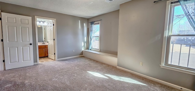 unfurnished bedroom featuring multiple windows, connected bathroom, light colored carpet, and a textured ceiling