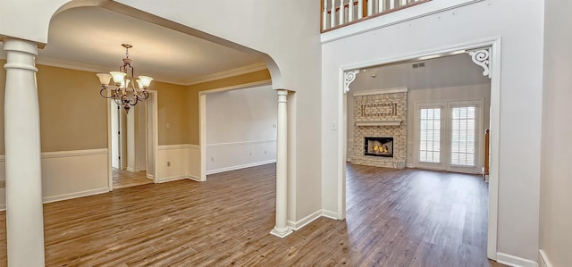 interior space featuring hardwood / wood-style floors, crown molding, a brick fireplace, and ornate columns