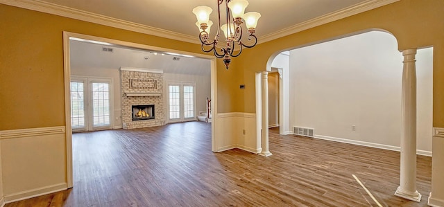 unfurnished living room with an inviting chandelier, ornamental molding, a fireplace, and ornate columns