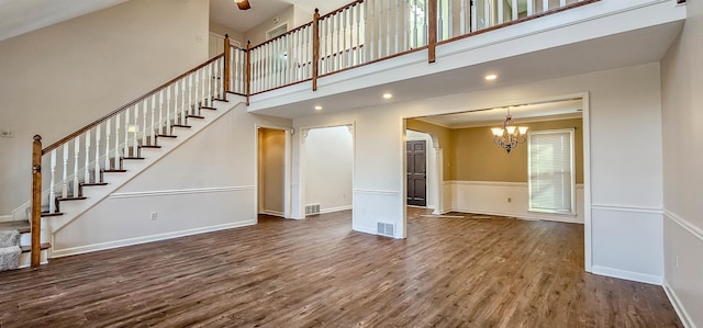 unfurnished living room with a high ceiling, ornamental molding, hardwood / wood-style floors, and an inviting chandelier