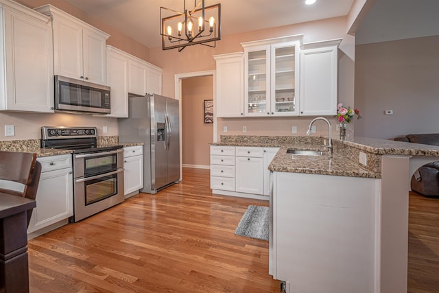 kitchen with sink, white cabinetry, hanging light fixtures, appliances with stainless steel finishes, and kitchen peninsula