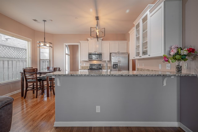 kitchen with appliances with stainless steel finishes, decorative light fixtures, white cabinets, kitchen peninsula, and an inviting chandelier