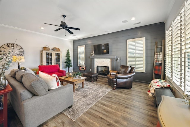 living room with a tiled fireplace, crown molding, wood-type flooring, and wood walls