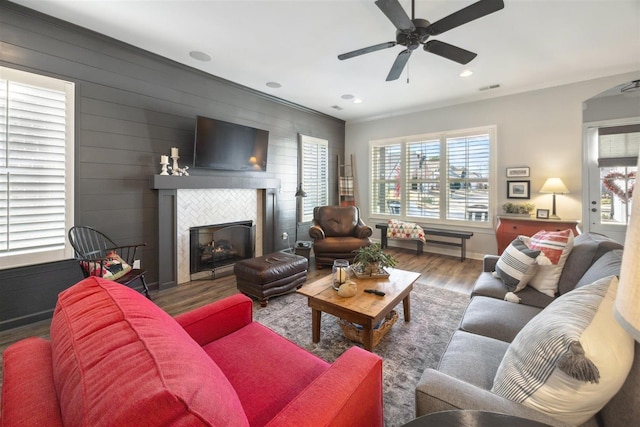 living room featuring ceiling fan, a fireplace, hardwood / wood-style floors, and wood walls