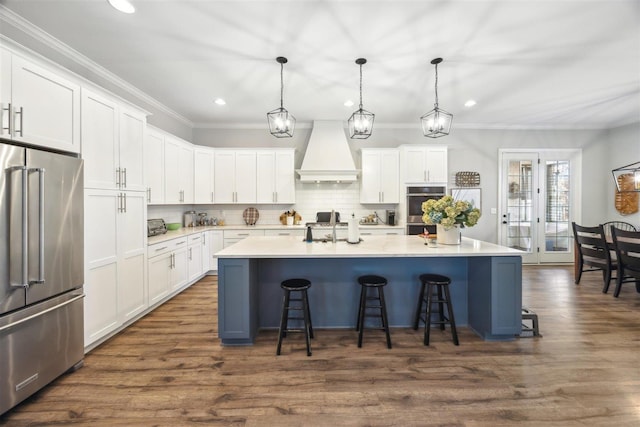 kitchen featuring a center island with sink, stainless steel appliances, white cabinets, and premium range hood