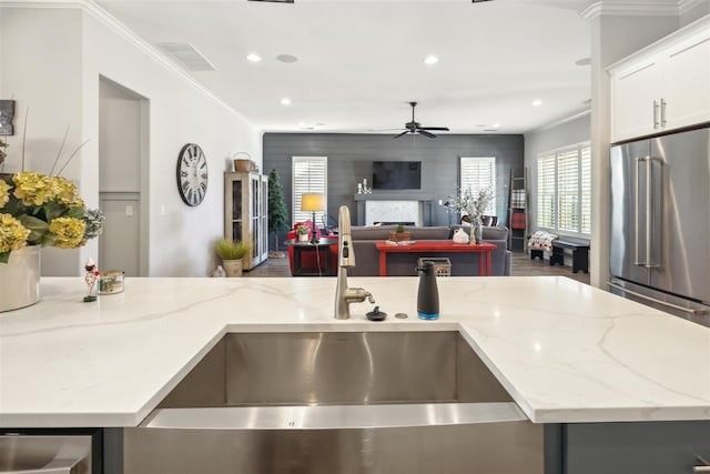 kitchen with light stone counters, white cabinetry, crown molding, and sink