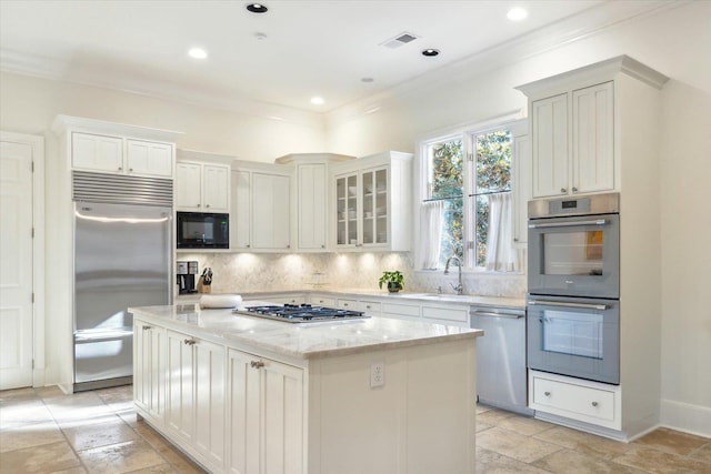 kitchen featuring sink, a center island, built in appliances, light stone counters, and tasteful backsplash