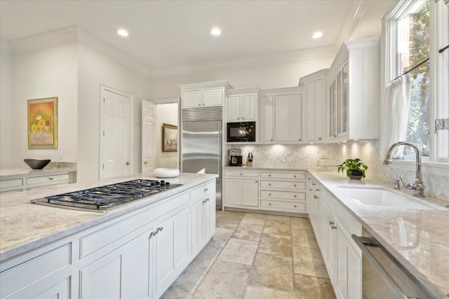 kitchen with sink, white cabinetry, light stone counters, built in appliances, and plenty of natural light