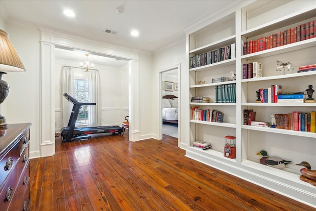 workout room with an inviting chandelier, ornamental molding, and dark hardwood / wood-style floors