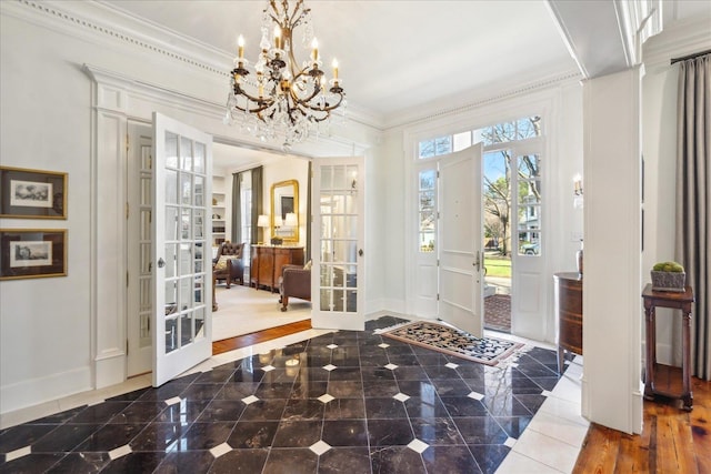 foyer entrance featuring ornamental molding, a chandelier, and french doors