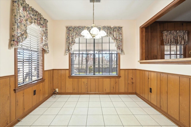 unfurnished dining area featuring a notable chandelier, wooden walls, and a wealth of natural light