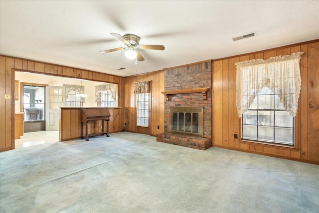 unfurnished living room with light carpet, a fireplace, plenty of natural light, and wood walls