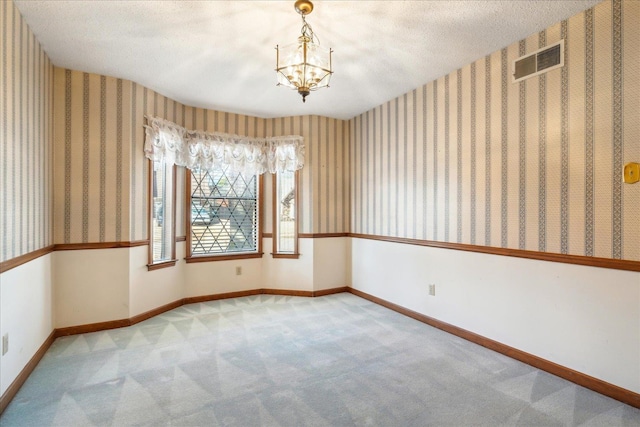 carpeted empty room with a notable chandelier and a textured ceiling