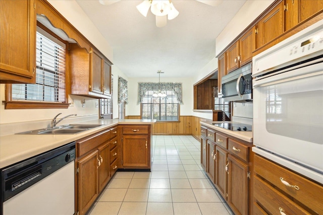 kitchen featuring sink, white appliances, hanging light fixtures, wooden walls, and kitchen peninsula