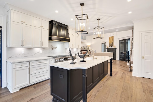 kitchen with premium range hood, decorative light fixtures, white cabinets, decorative backsplash, and a kitchen island with sink