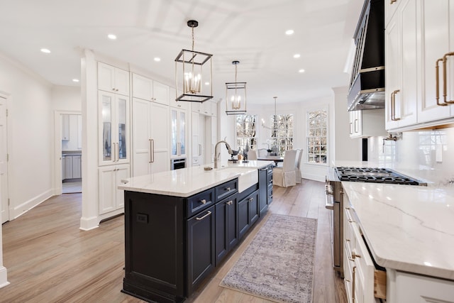 kitchen featuring pendant lighting, sink, white cabinetry, stainless steel gas stove, and a center island with sink