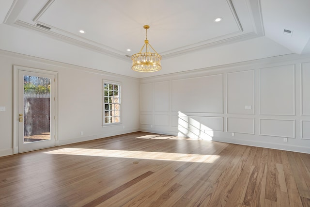 spare room with a raised ceiling, a chandelier, and light hardwood / wood-style flooring