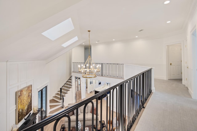 hallway with an inviting chandelier, ornamental molding, vaulted ceiling with skylight, and light carpet