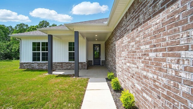 property entrance featuring brick siding, a shingled roof, and a yard